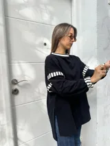 Buzo oversize de color negro con detalles de rayas blancas y negras en el cuello, puños y hombros. Presenta un pequeño parche bordado en el pecho.