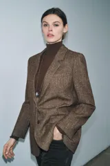 Blazer de Zara confeccionado en hilatura con lana, con diseño de espiga en tonos marrones. Presenta cuello solapa, manga larga con botones, bolsillo de vivo en el pecho y bolsillos delanteros con solapa. Cierre frontal con botones y forro interior negro.