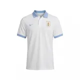 Polo de la Selección Uruguaya de Fútbol marca Nike, color blanco con cuello y bordes de mangas en celeste. Presenta el logo de la marca bordado en el pecho derecho y el escudo de la AUF en el pecho izquierdo.