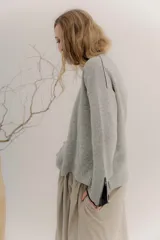 Buzo de lambswool color beige, con escote redondo y detalle en V. Presenta cierres metálicos en los puños que revelan un interior en contraste de color marrón y ribete rojo. Tiene tajos laterales para mayor comodidad y un fit amplio.