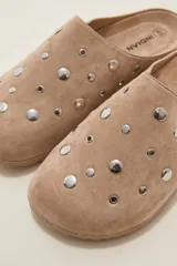 Suecos tipo zueco color negro con acabado de gamuza, decorados con tachas metálicas plateadas circulares. Poseen suela plana y diseño abierto en el talón.