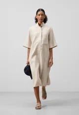 Vestido largo de lino color crema con finas rayas verticales. Tiene cuello mao, mangas cortas anchas, botonadura frontal oculta y un bolsillo en el pecho.