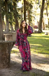 Vestido largo de lino con escote cruzado, mangas largas abullonadas y lazo ajustable en la cintura. Presenta un estampado floral vibrante en tonos fucsia, violeta y verde.