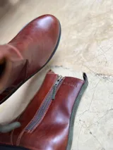 Botas de cuero marrón con suela de goma track y doble cierre lateral con tiradores de gamuza. Cuenta con presilla trasera y detalle de panel posterior en gamuza a contratono.