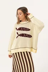 Sweater color manteca de tejido de punto con cuello redondo y ribete marrón. Presenta dos peces marrones tejidos en el frente con detalles bordados a mano.