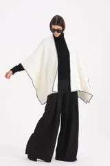 Spolverino abierto de corte amplio, color blanco con bordes en contraste de costura negra. Presenta un diseño envolvente tipo capa con mangas integradas.