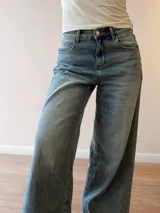 Pantalón de jean con corte wide leg y tiro medio-alto. Presenta un lavado gris azulado desgastado con acabado vintage y ruedo desflecado.