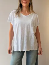 Remera de lino y algodón color beige con escote en V, mangas cortas y calce relajado. Presenta un bolsillo frontal decorado con apliques de strass, encaje y tachas, además de sutiles estampas con escritura manuscrita y detalles desflecados.