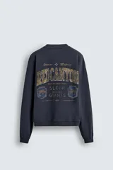 Sudadera de manga larga, cuello redondo y corte cropped, color azul marino oscuro con efecto lavado. Presenta un estampado frontal en tonos dorados y desgastados con el texto "RED CANYON" y las palabras "Granite" y "Majesty" flanqueando un símbolo de cruz.