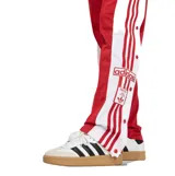 Pantalon deportivo Adidas modelo Adibreak, color rojo con franjas laterales blancas y las icónicas tres tiras en rojo. Presenta botones a presión a lo largo de los laterales y cintura elástica.