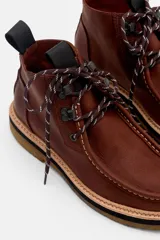 Borcego de cuero color marrón con diseño de costuras tipo mocasín en la puntera, cordones jaspeados y suela de goma con plataforma en capas.