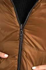 Campera reversible con diseño acolchado, cierre frontal y capucha. Un lado es de color negro y el otro de color tostado, con puños tejidos en color negro.