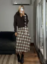 Pollera midi de corte recto con tajo lateral, confeccionada en tela con estampado escocés en tonos marrones, blancos y negros.