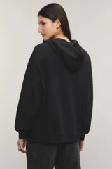 Buzo hoodie oversize negro, confeccionado en rústico de algodón y poliéster, con capucha, bolsillo tipo canguro y detalle de estampa de botas vaqueras con tachas en el centro del pecho.