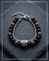 Pulsera doble de acero inoxidable con piedras naturales de ónix negro y piedras jaspeadas en tonos tierra, unidas por un cierre cilíndrico metálico con textura estriada.