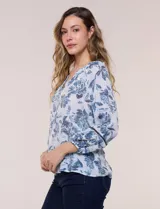 Blusa holgada de rayón y poliéster, marca Zac & Rachel, con estampado floral en tonos azules sobre fondo blanco. Posee escote en V con muesca central, mangas largas abullonadas con inserción de puntilla y puños elastizados.