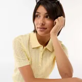 Remera de punto calado color amarillo, con cuello polo, manga corta y cierre frontal parcial con botones.