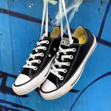 Championes urbanos Converse Chuck Taylor All Star de caña baja, color negro con detalles en blanco, confeccionados en lona, con suela de goma y logo de la marca en la lengüeta y el talón.