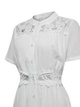 Vestido midi blanco de lino orgánico y viscosa, con cuello mao, mangas cortas y cierre frontal de botones. Presenta detalles de encaje en los hombros, el pecho y la cintura.