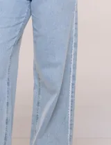 Pantalón jean de tiro alto y corte wide leg en color celeste, con detalle de puntilla en los laterales. Cuenta con cinco bolsillos, presillas para cinto y cierre frontal con botón.
