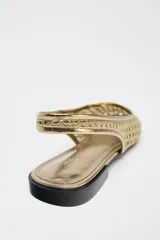 Zapato plano destalonado tipo bailarina color dorado, con efecto metalizado y detalle trenzado en el corte. Estilo mule con tira trasera con pieza elástica. Suela de 1,5 cm de altura.