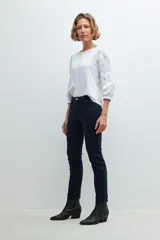 Pantalón de denim negro, corte slim, con cintura media y cierre frontal con botón y cremallera.