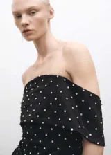 Vestido corto de fiesta en tejido satinado negro, con diseño entallado y escote palabra de honor con solapa vuelta. Presenta apliques decorativos brillantes distribuidos por toda la prenda y cierre de cremallera en la parte posterior.