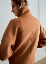 Abrigo corto de paño en color camel, con cuello alto, cierre frontal de botones y bolsillos laterales con solapa. Presenta un diseño de corte recto y estructura holgada.