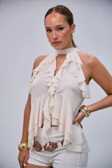 Blusa sin mangas de color crudo con cuello halter y abundantes volados en la parte frontal y sisas.