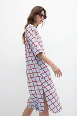 Maxi vestido camisero celeste con estampado geométrico de cuadrados rojos, mangas cortas y aberturas laterales.