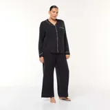 Conjunto de pijama de dos piezas compuesto por una camisa de manga larga con botones frontales y cuello solapa, y un pantalón de corte recto. Ambas prendas presentan un diseño liso en color negro con detalles de ribetes en contraste.