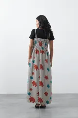 Vestido midi de corte fluido con cuerpo superior fruncido, escote recto y tiras finas regulables. Presenta un diseño estampado con hojas en tonos rojos y turquesas sobre una base de rayas verticales finas.