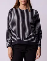 Blusa de gasa estampada con líneas verticales negras sobre fondo beige, de manga larga con puño abotonado. Espalda con abertura y botón.