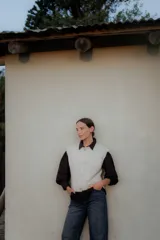 Chaleco de punto en color crudo, con cierre frontal de botones decorativos en forma de sol, cuello redondo y diseño sin mangas.