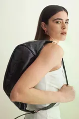 Cartera tipo medialuna de cuero brillante, con cierre de cremallera superior y correa extraíble con herrajes dorados.