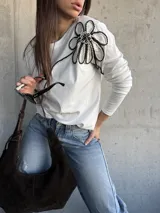 Remera blanca de manga larga con diseño de flor grande aplicada en relieve con cordón negro y blanco sobre el hombro izquierdo.