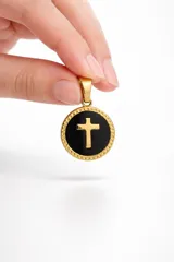 Dije circular de acero dorado con centro esmaltado en negro y cruz dorada en relieve, con borde texturizado.