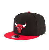 Gorra New Era modelo 9FIFTY de visera plana, color negro con visera y botón superior rojos. Presenta el logotipo bordado de los Chicago Bulls en el frente.