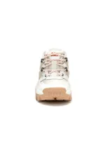 Sneakers Cat modelo Reactor, de diseño robusto estilo trekking, en color blanco con detalles en beige y suela chunky de goma marrón claro. Presenta cordones estilo montaña y apliques laterales de refuerzo.