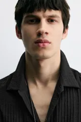 Camisa de corte relajado confeccionada en tejido fluido con textura acanalada. Presenta cuello solapa, manga corta y cierre frontal con botones.