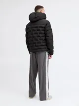 Campera puffer negra con capucha ajustable, cierre frontal y bolsillos laterales. Presenta un diseño acolchado con textura geométrica en el frente, puños con ajuste de velcro y logo sutil en el pecho.