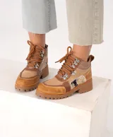 Borcego de cuero color marrón con paneles de tela texturizada y estampado animal print. Tiene cordones marrones, herrajes metálicos y suela de goma con plataforma.