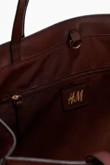 Cartera tote color bordó con doble asa de mano y correas de hombro finas. Cuenta con cierre de mosquetón en el interior y compartimento interior con cierre.