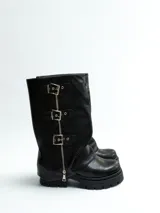 Bota de caña media de ecocuero color negro, con suela track, cierre lateral y tres hebillas decorativas con cierre de cremallera frontal.