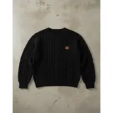 Sweater de punto color crema con diseño de trenzas y rombos, cuello redondo y mangas largas. Presenta un pequeño aplique decorativo en el pecho.
