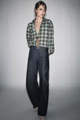 Camisa de corte oversize confeccionada en algodón, con estampado de cuadros en tonos verde, negro y blanco. Presenta cuello solapa, cierre frontal con botones, manga larga con puños y bajo asimétrico.