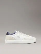 Zapatillas de corte bajo Calvin Klein, con diseño minimalista en color blanco y beige. Presentan una combinación de materiales en la capellada, incluyendo piel y ante, con detalles en contraste en el talón y logo de la marca en el lateral y la mediasuela.