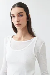 Remera de manga larga, color blanco roto, con cuello bote y textura acanalada. Presenta un efecto de doble capa o transparencia sutil en el escote.