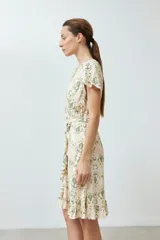 Vestido corto cruzado con estampado abstracto en tonos verde oliva, amarillo y rosa. Tiene escote en V, mangas cortas con volados y falda con volados en el ruedo. Se ata a la cintura con un lazo.