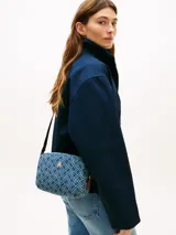 Cartera cruzada estilo cámara de Tommy Hilfiger, confeccionada en denim de algodón con estampado de monograma TH y detalles en cuero vacuno. Cuenta con cierre principal y herrajes metálicos dorados, incluyendo el monograma TH en el frente. Posee correa ajustable y extraíble.